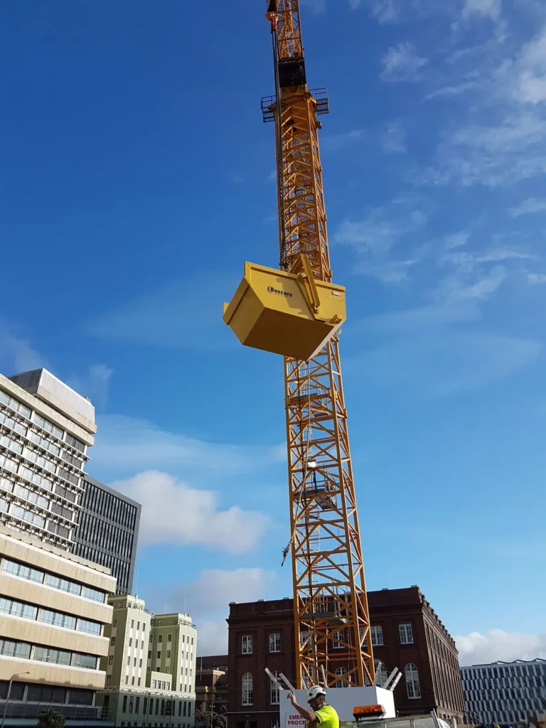 materials handling skip in the air with a crane behind it next to a building