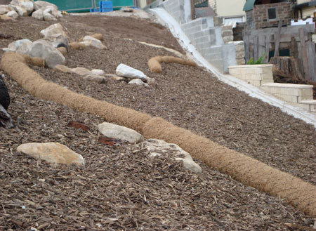 Coir log on a hill with bark and other absorbents preventing sediment from entering unwanted areas