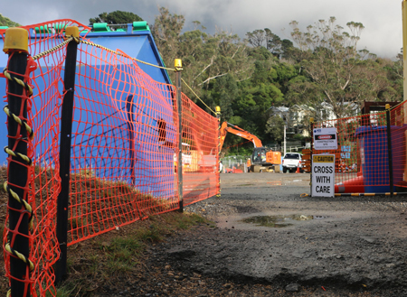 Orange barrier mesh with danger and directional signage at a busy construction site