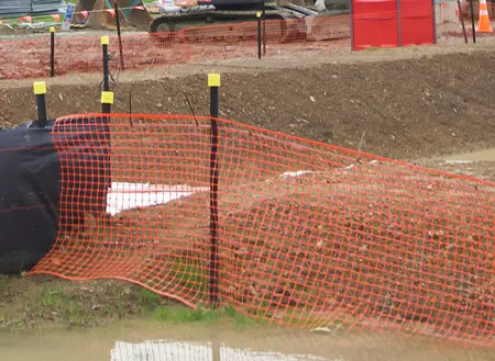 Bright orange barrier mesh fence with waratah and bright yellow safety cap on a muddy civil construction site